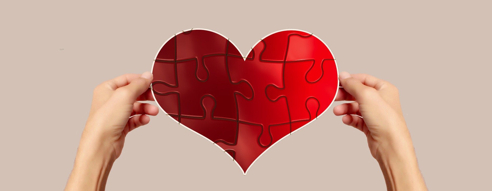 Ein Herz aus Puzzlestückchen wird von 2 Händen gehalten